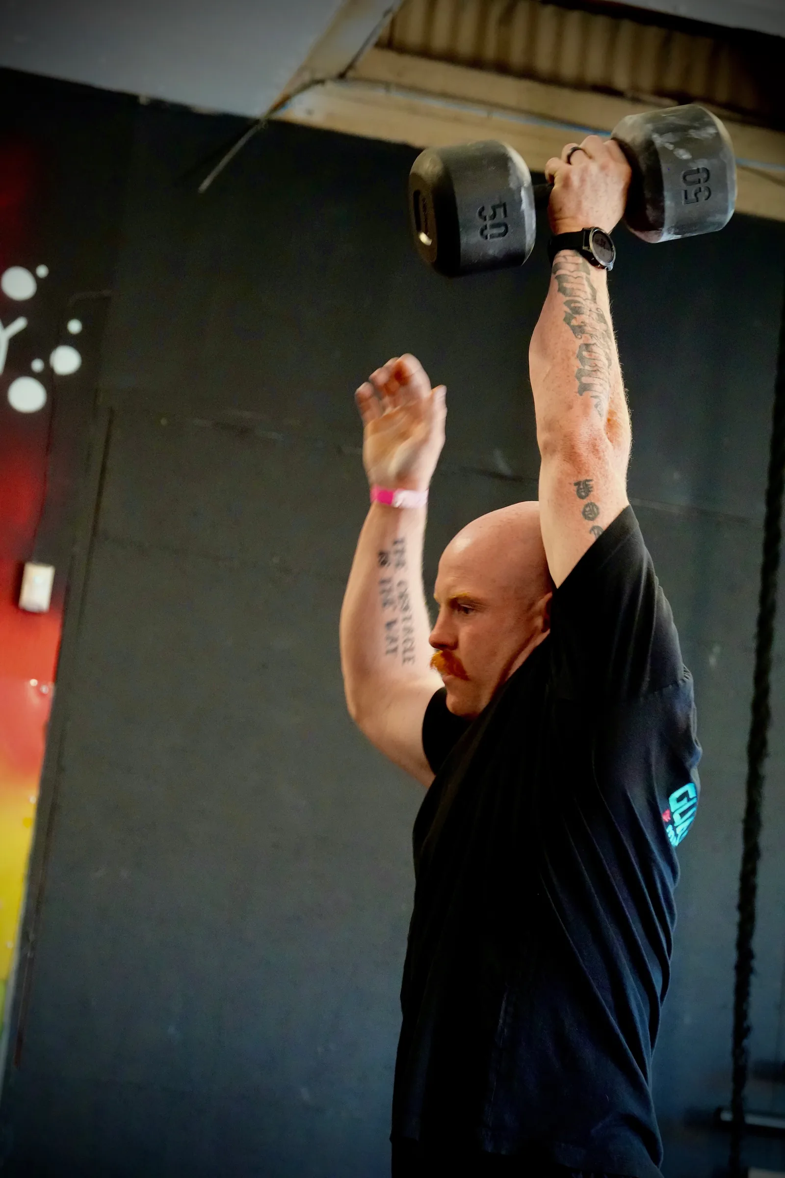 Taylor pressing a heavy dumbbell overhead in the gym.