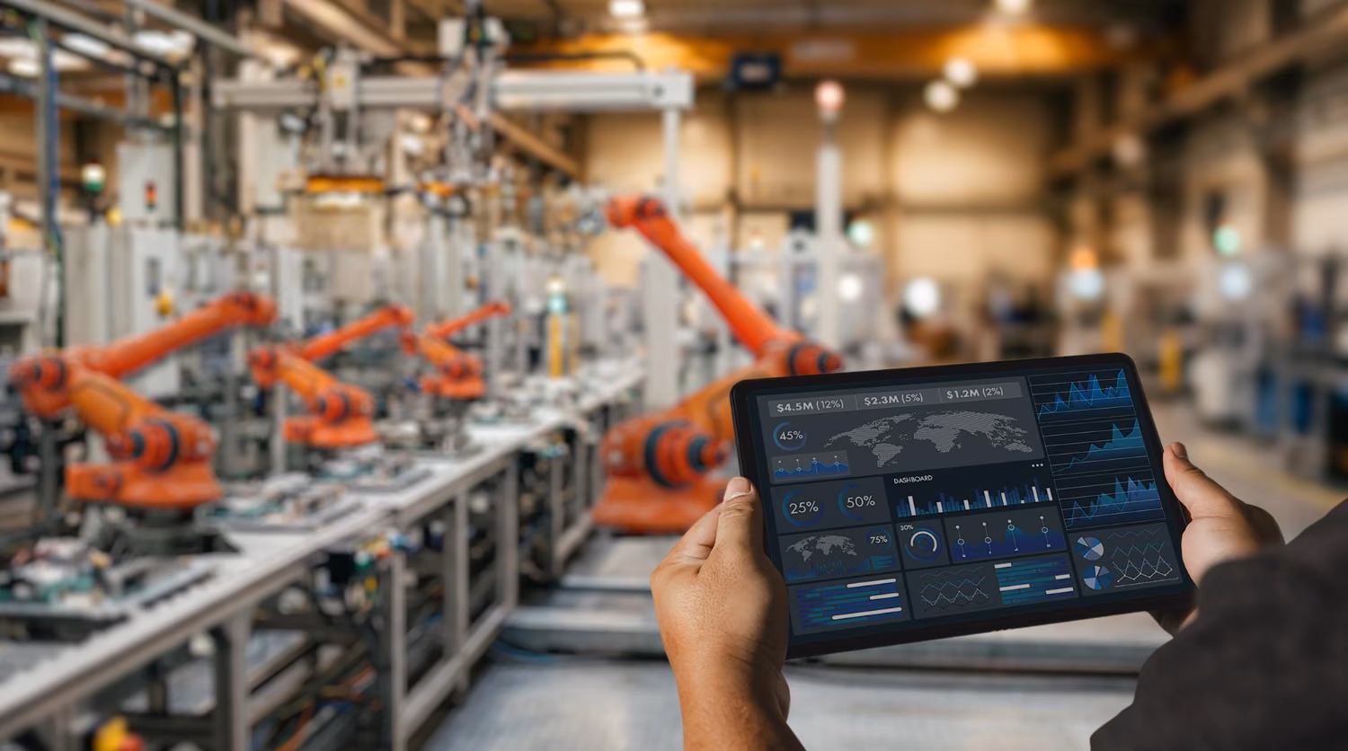 Tablet z wykresami na tle robotów na hali produkcyjnej