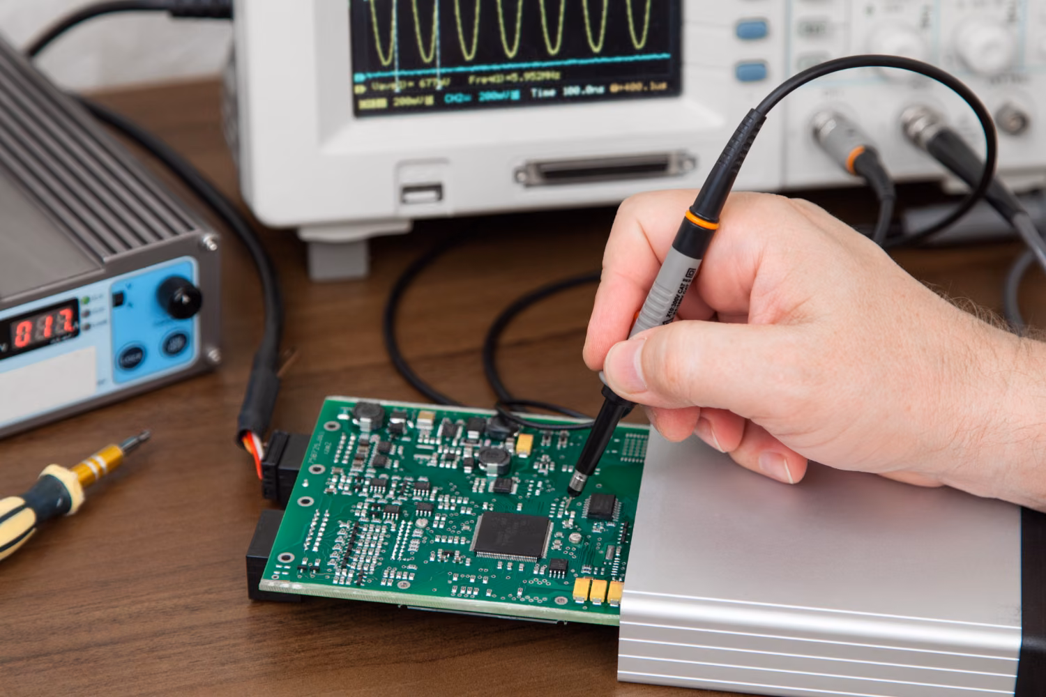 Sonda pomiarowa przy płytce PCB z oscyloskopem w tle