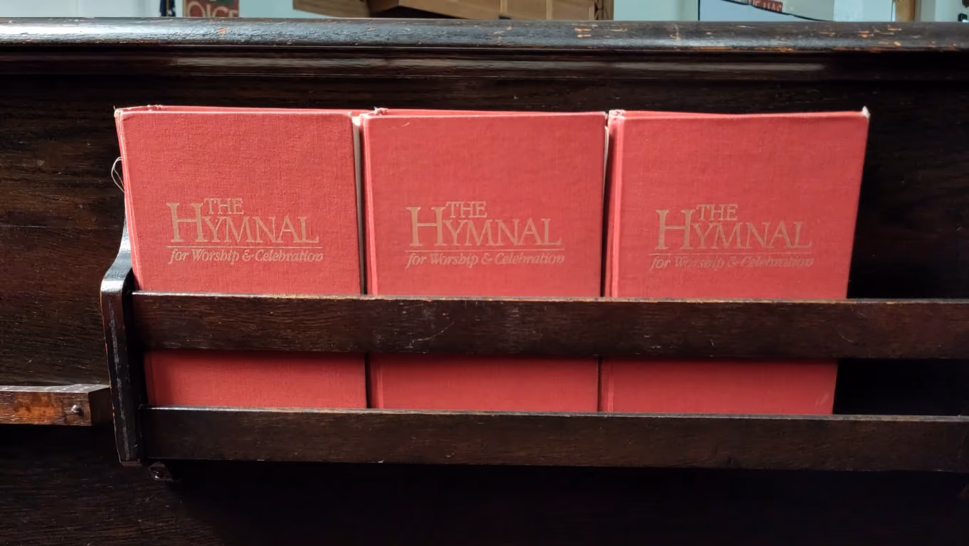 Three hymnals are stood up on the back of a pew.