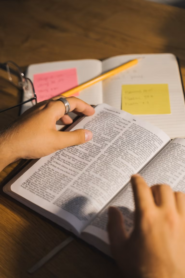 A man is reading a Bible while taking notes.