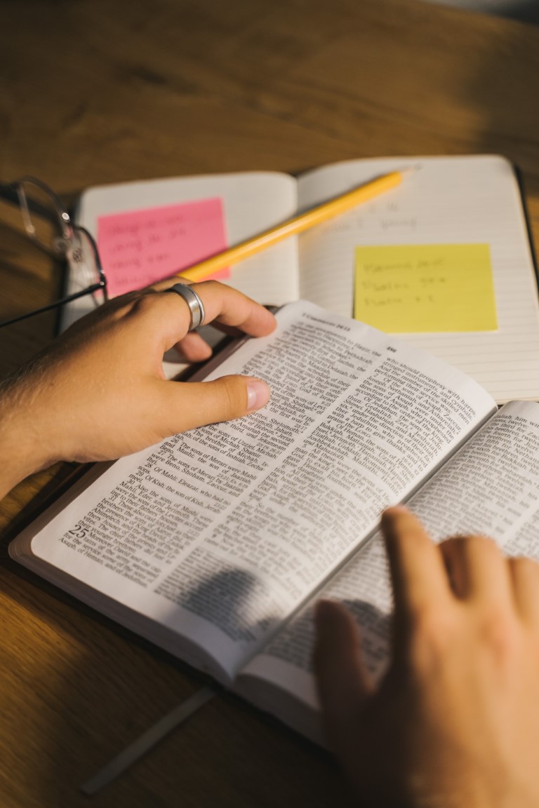 A man is reading a Bible while taking notes.