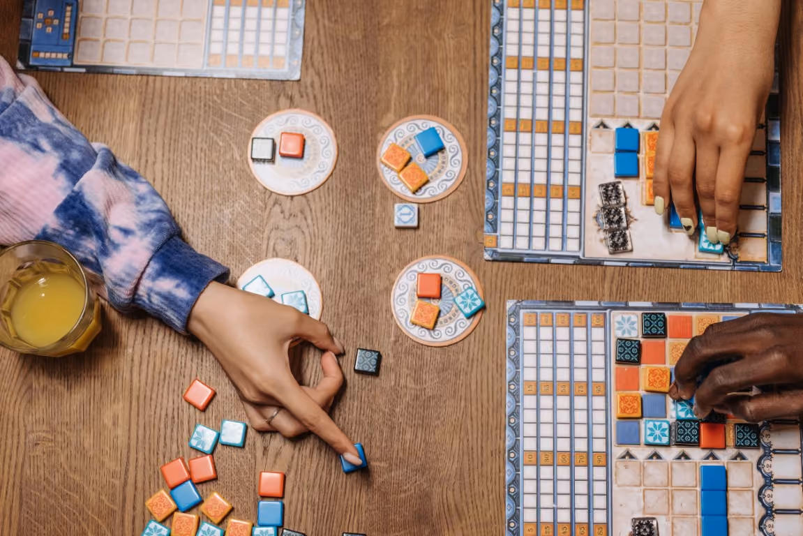 Three hands are interacting with a board game on top of a table.