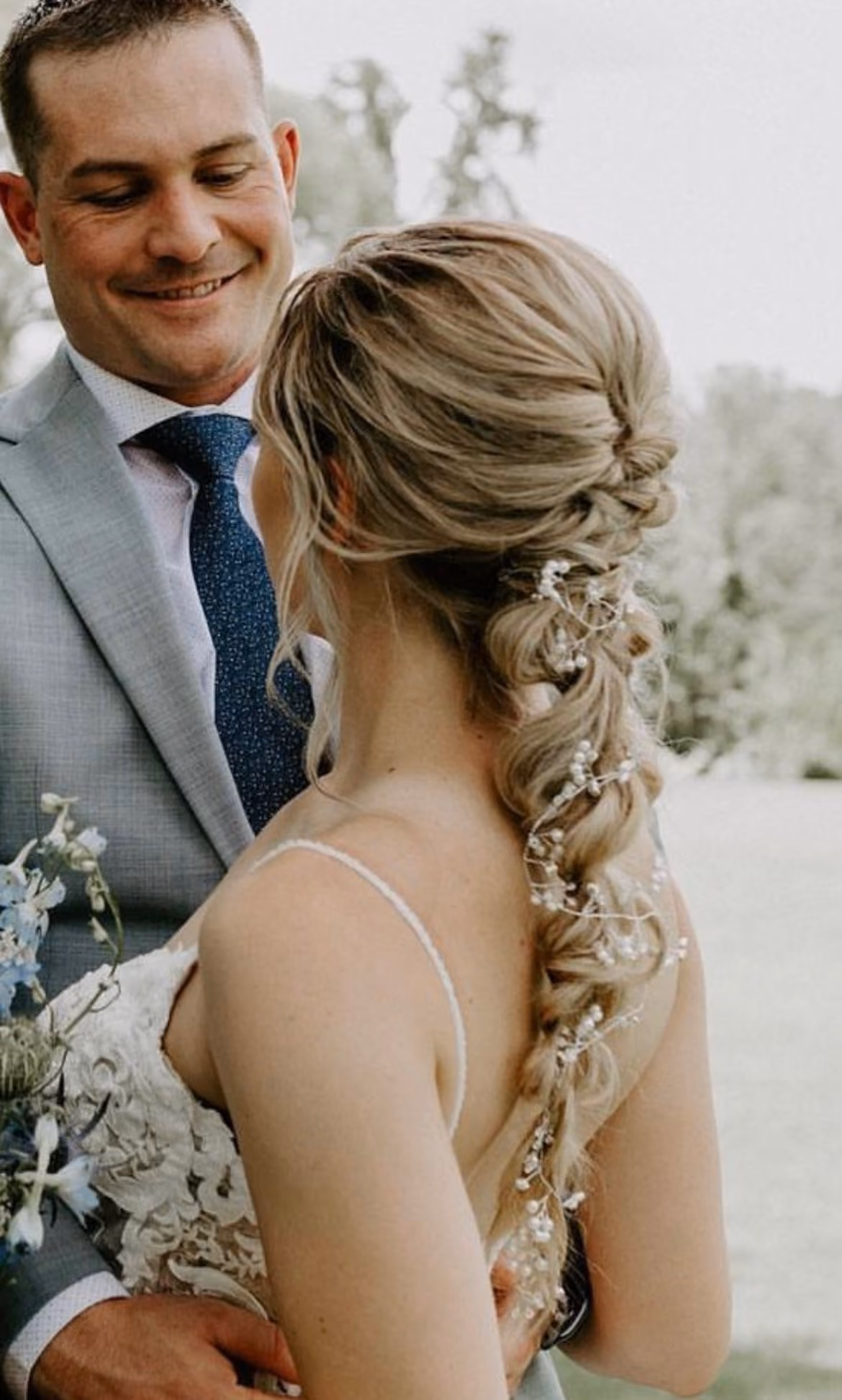 Groom embracing his bride, who wears a long braided bridal updo