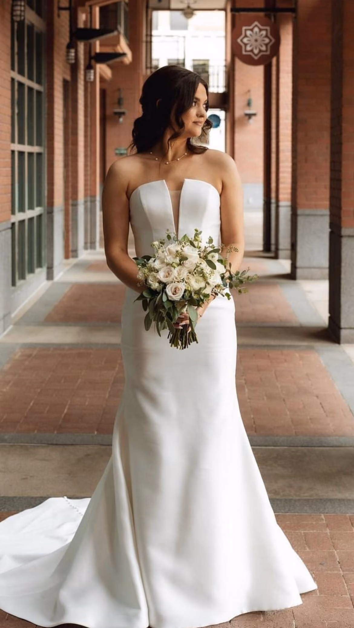 Bride in a strapless gown holding her bouquet in a brick archway