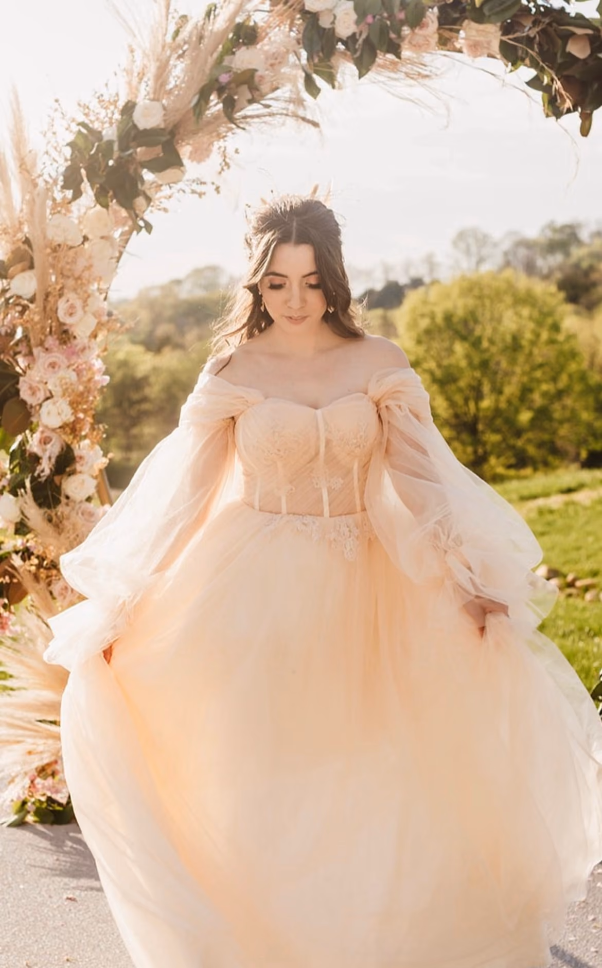 Bride in a blush tulle gown beneath a floral ceremony arch