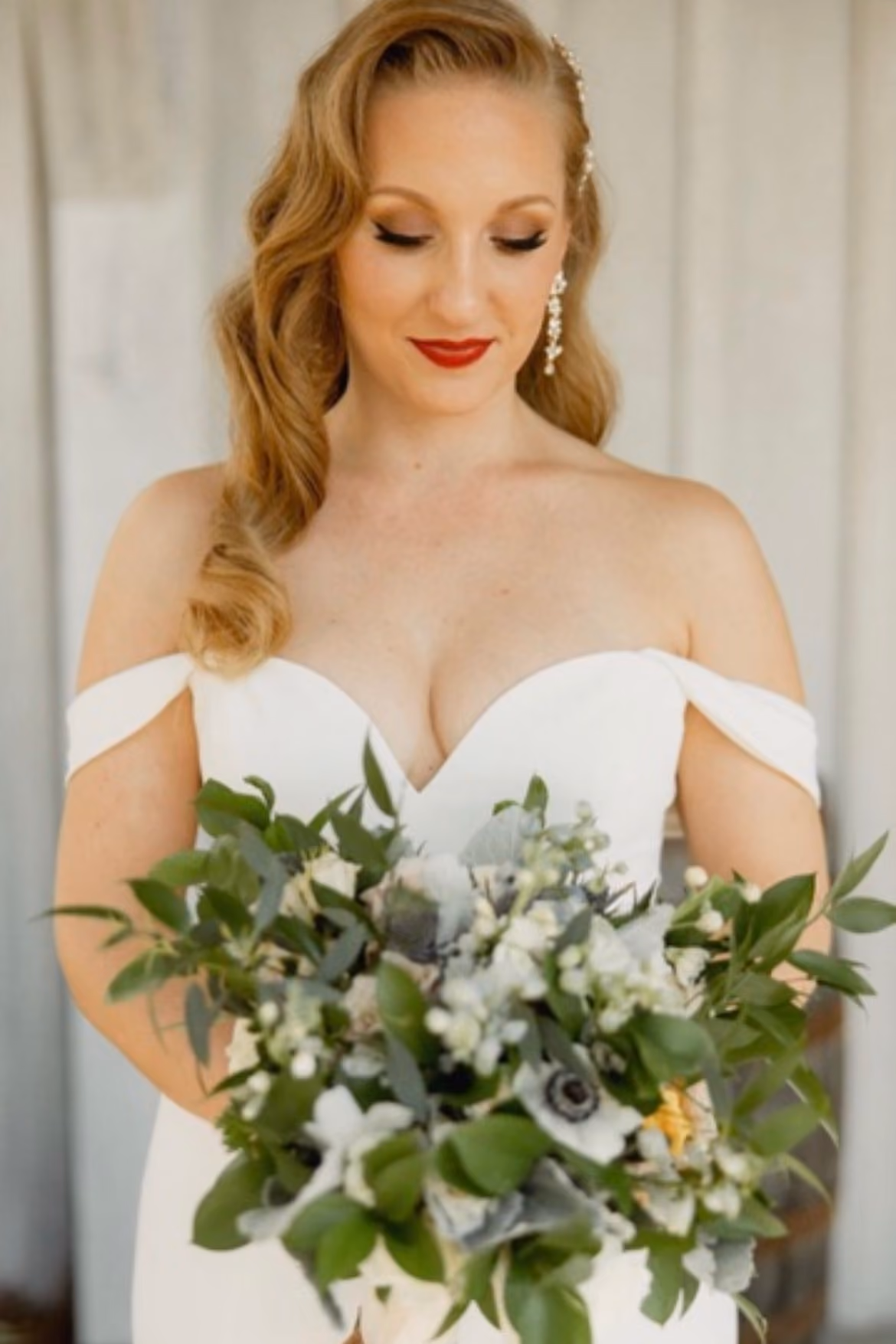 Bride with a side-swept curled style holding a white and eucalyptus bouquet