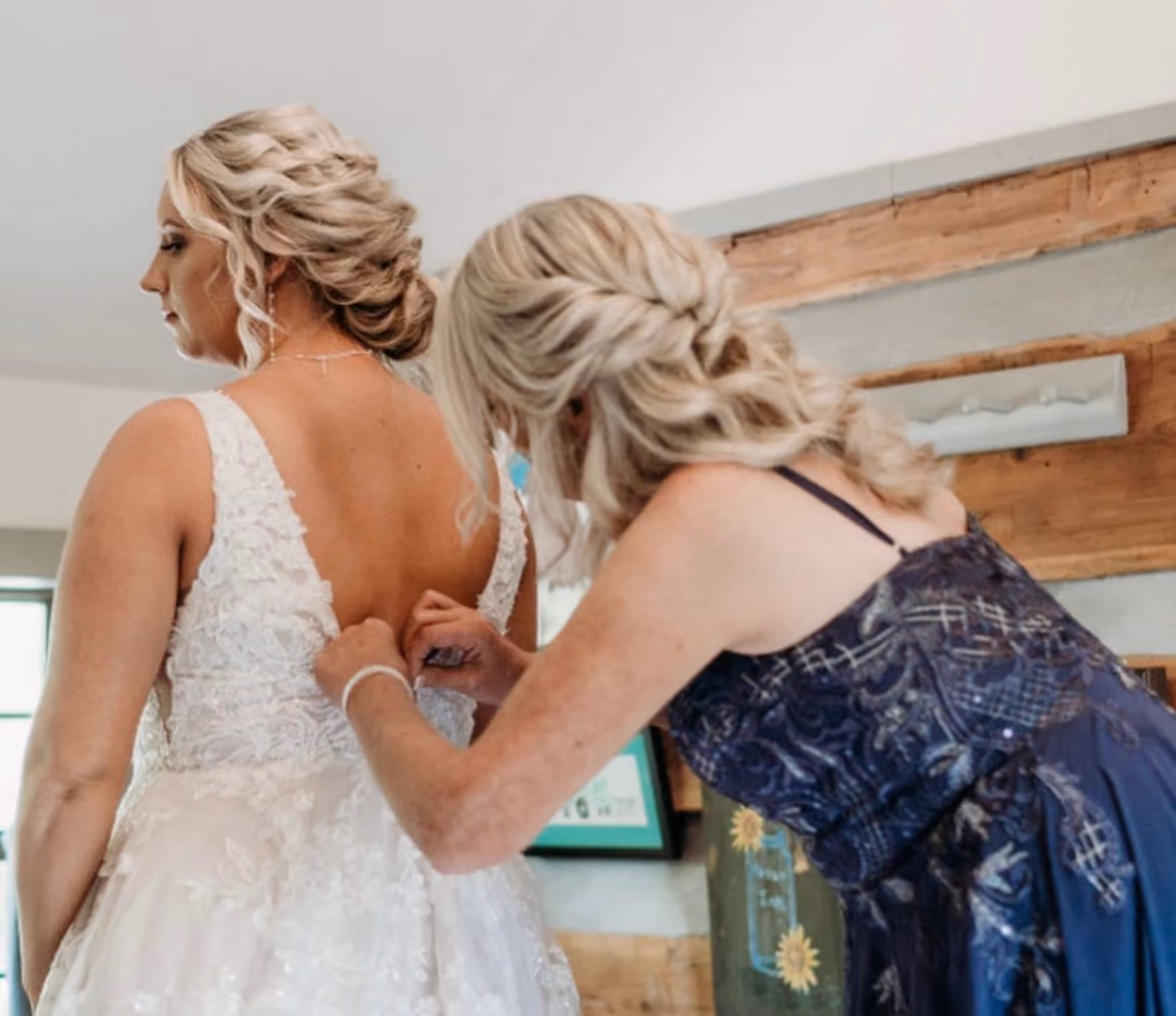 Bridesmaid buttoning the bride's lace gown before the ceremony