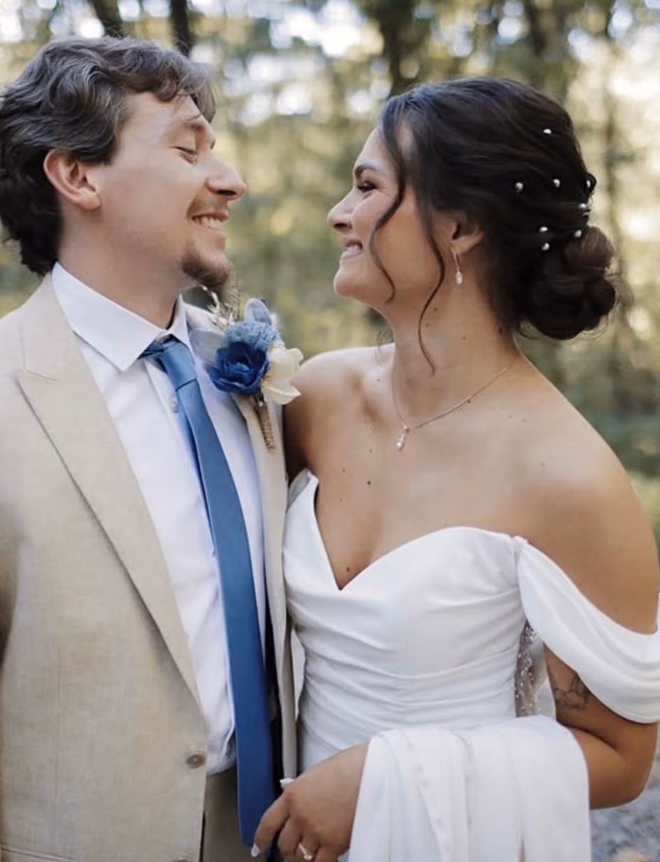 Bride and groom smiling at each other, her hair in a pinned updo with a jewelled comb