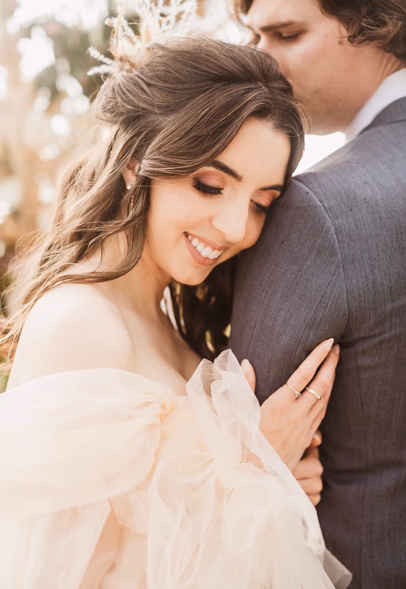 Bride smiling in a blush tulle gown as her groom holds her