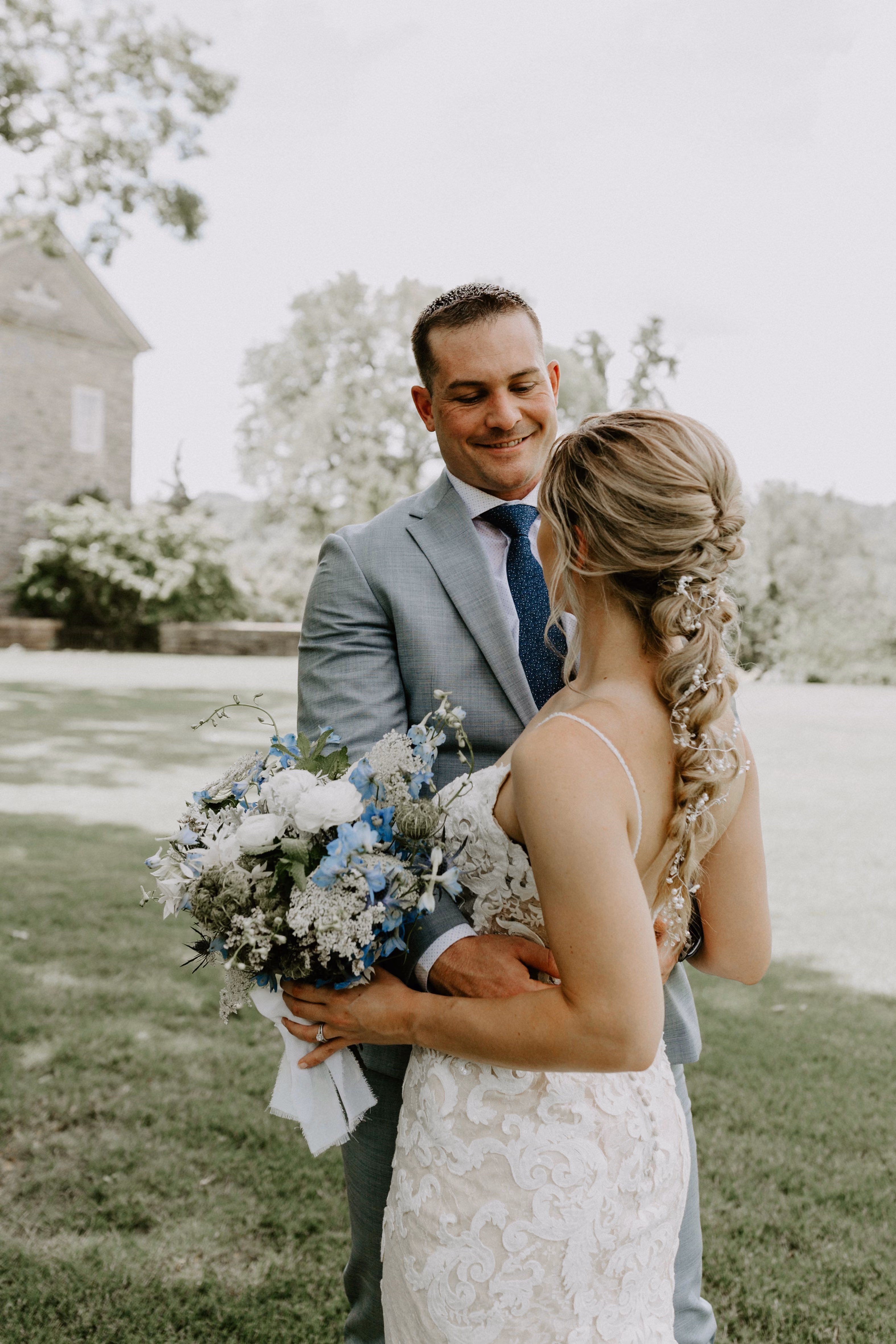 Bride with a long braided ponytail embracing her groom outdoors