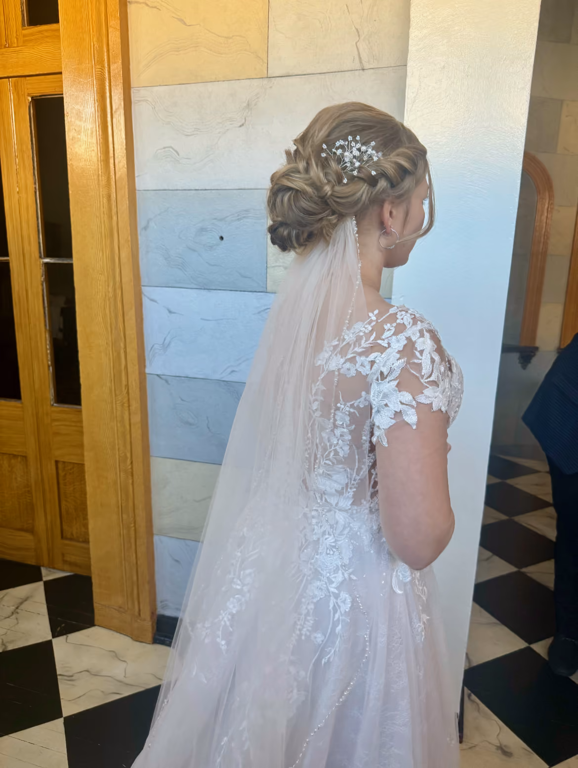 Back view of a bride's braided updo finished with a jewelled hairpiece and veil