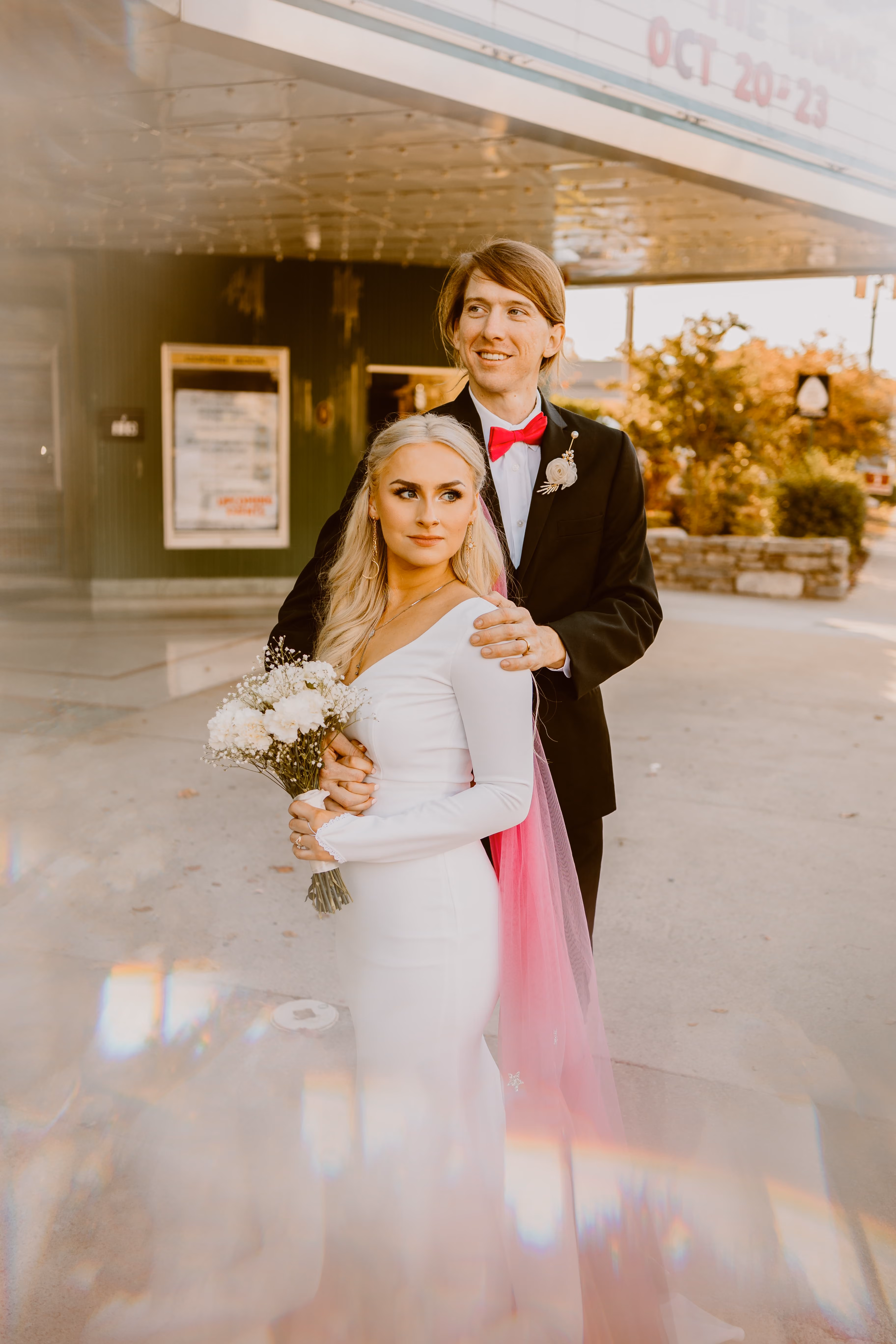Bride and groom outside a theatre marquee, her veil trailing behind