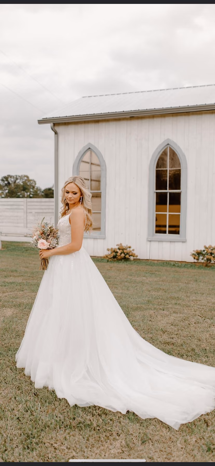 Bride with a long train standing outside a white chapel