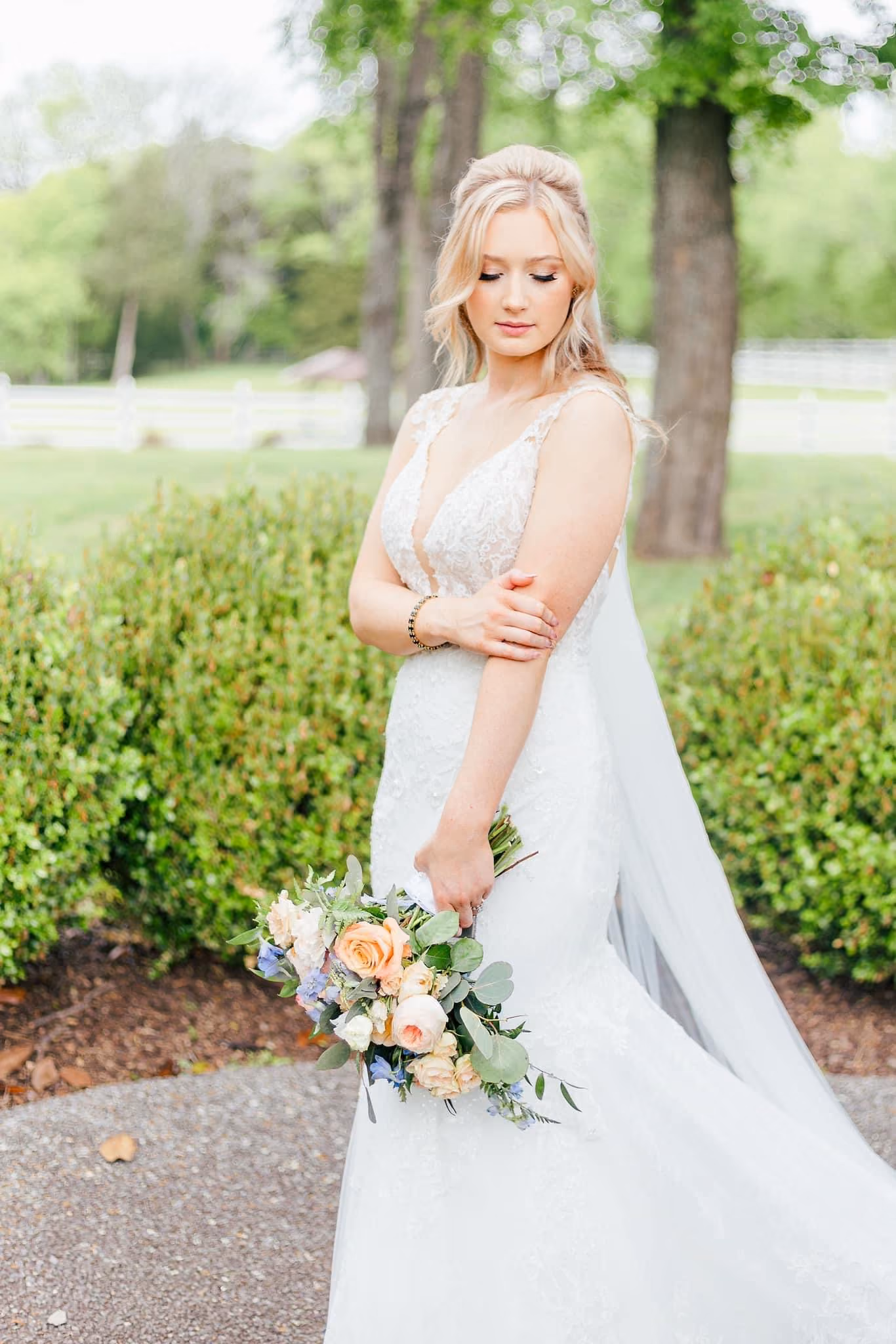 Bride in a lace gown holding a peach and cream bouquet in a garden