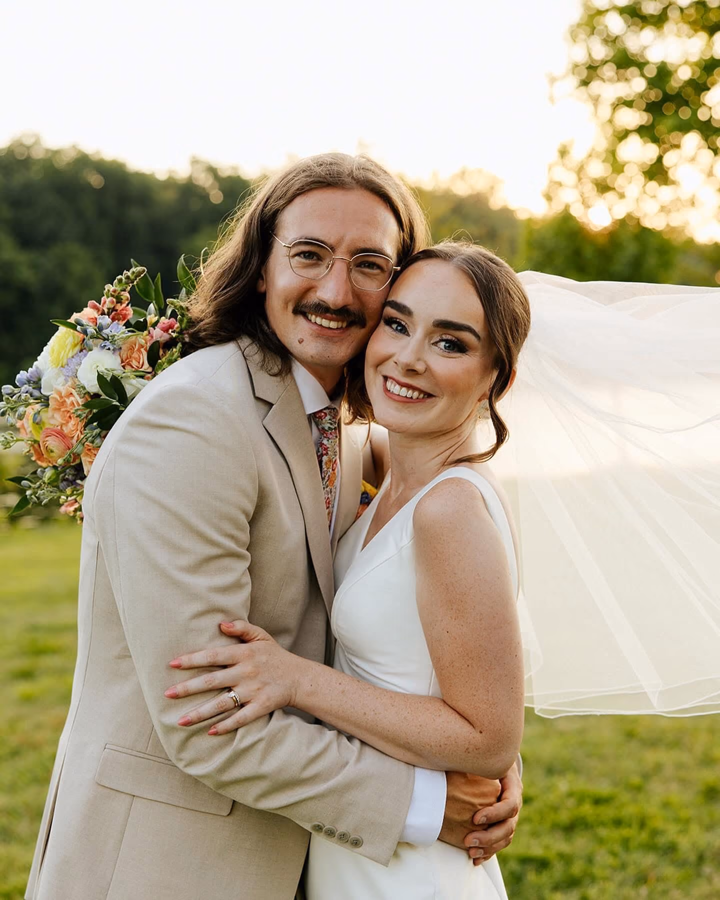 Bride and groom embracing outdoors as her veil catches the breeze