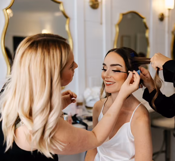 Hair stylist and makeup artist working on a bride together before the ceremony