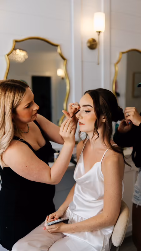 Makeup artist applying finishing touches to a bride in the getting-ready suite