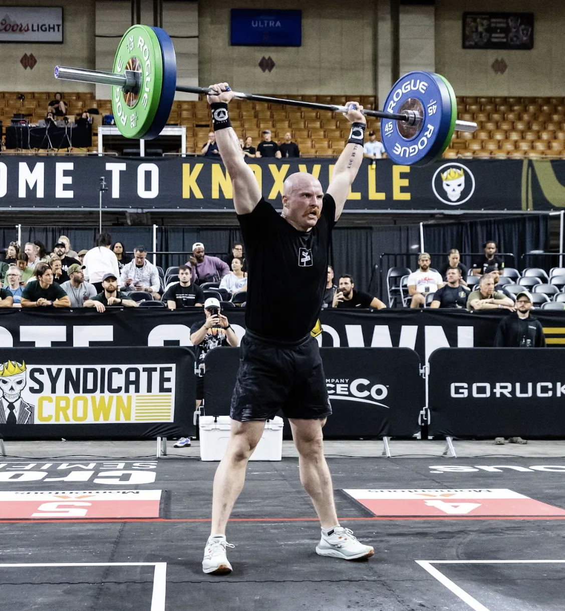 Taylor locking out a barbell overhead on the competition floor at the Syndicate Crown in Knoxville.