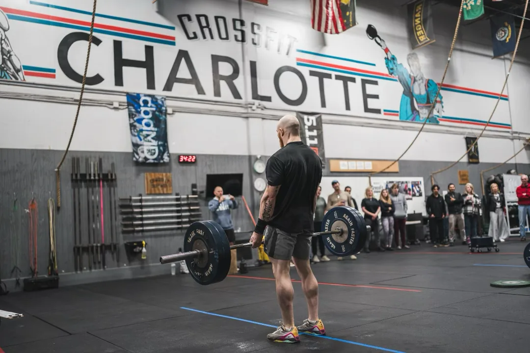 Taylor standing over a barbell in front of the CrossFit Charlotte wall mural with spectators watching.