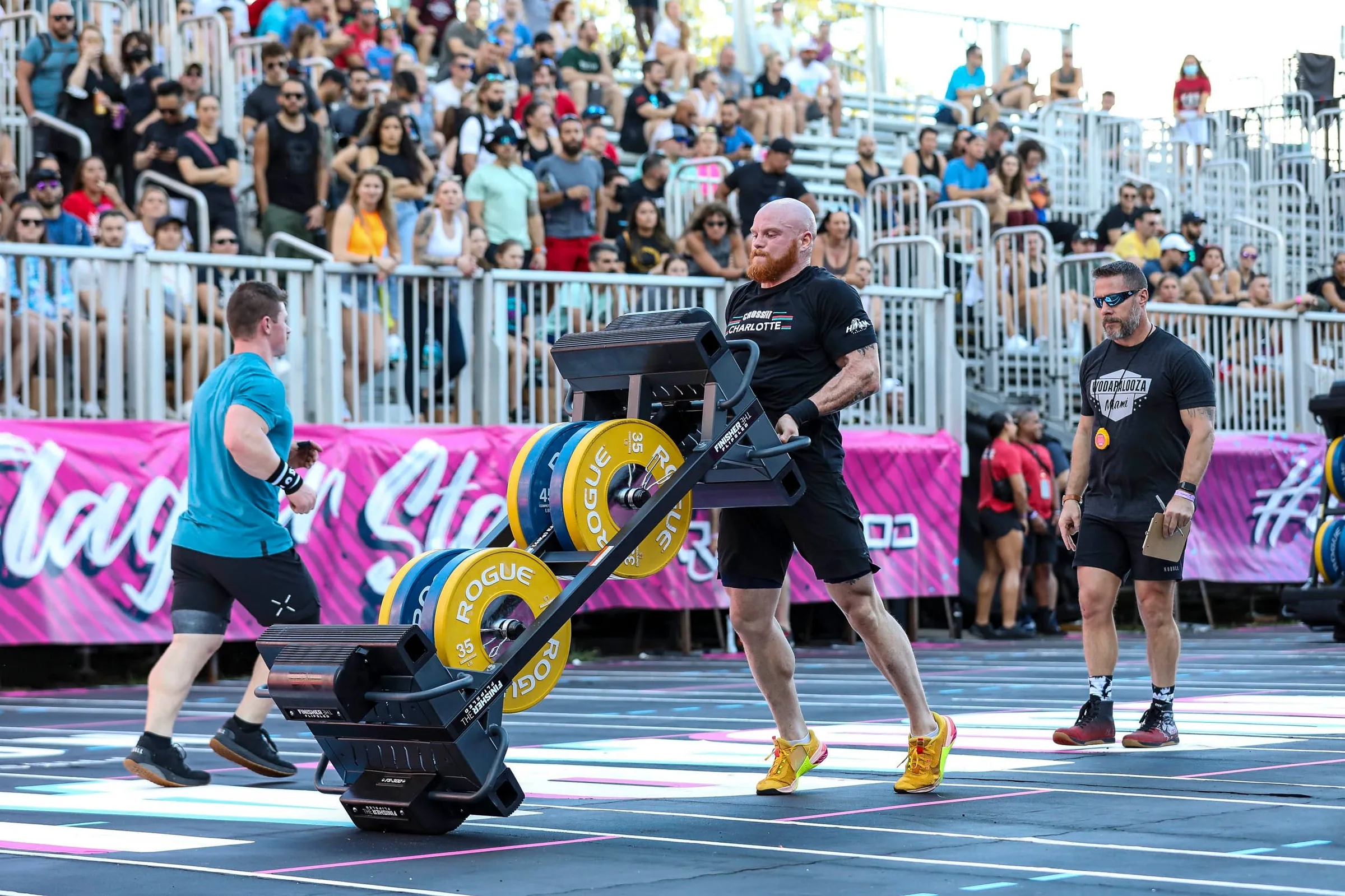 Taylor driving a loaded sled across an outdoor competition floor in front of the stands.