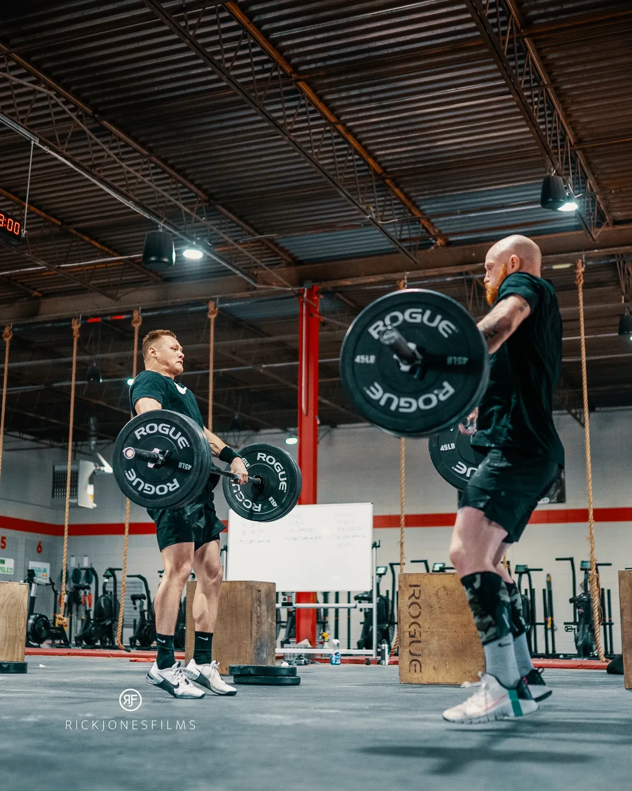 Taylor and a training partner cleaning loaded barbells side by side during a training session.