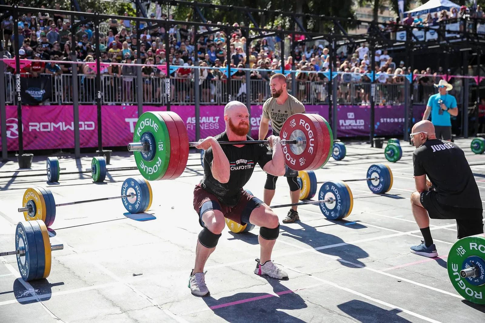 Taylor standing up a heavy squat clean on an outdoor competition floor as a judge watches.
