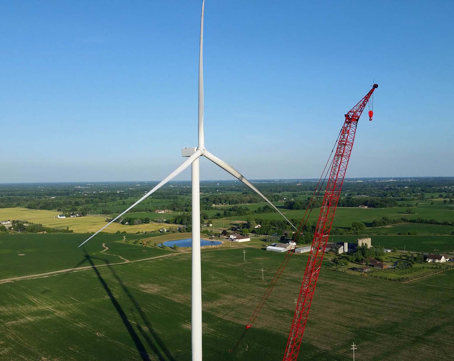 Green John Deere agricultural machine in a field with wind turbines against a clear blue sky.