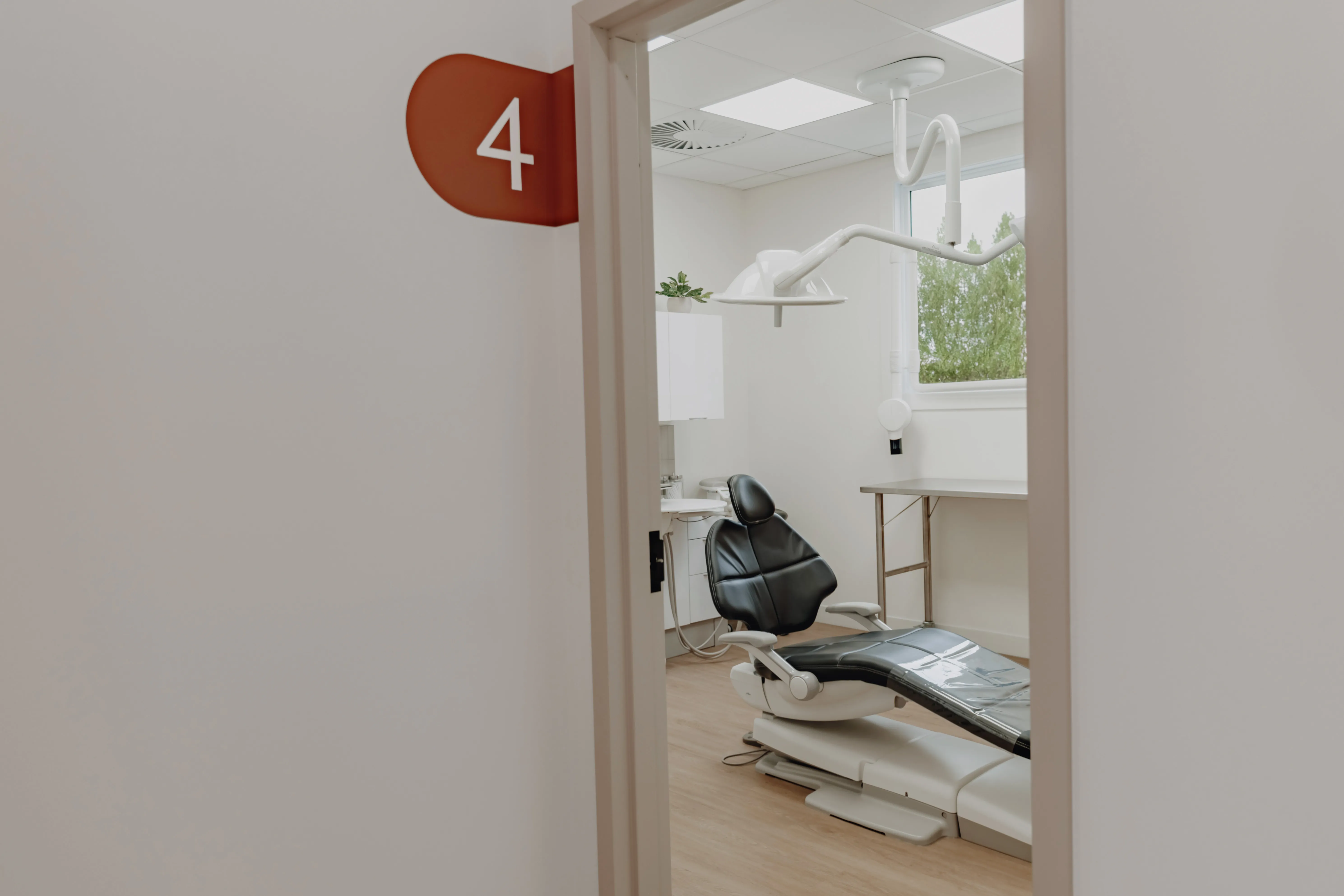 Porte ouverte de la salle de soins numéro 4, avec un fauteuil dentaire noir et une lampe de traitement