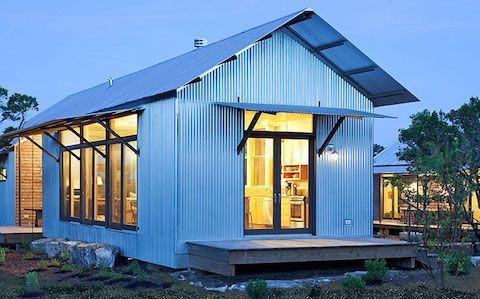 Blue steel-clad cabin lit from within at dusk.