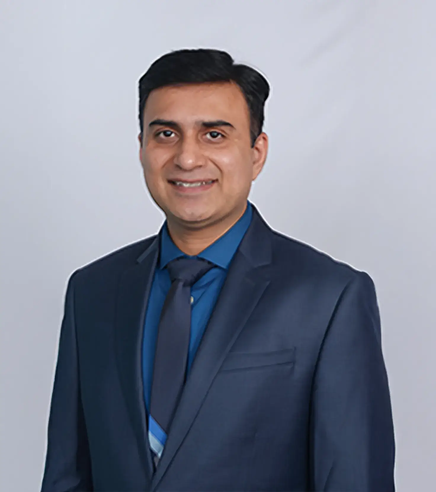 Smiling man wearing a dark blue suit, blue shirt, and matching tie against a neutral background.