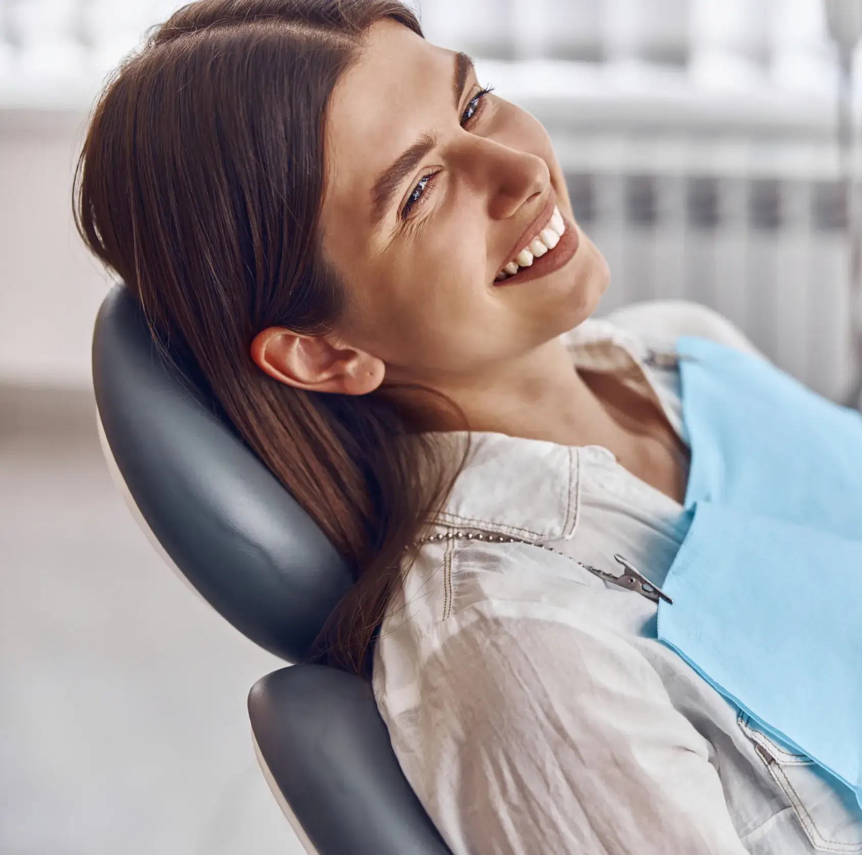Woman smiling while sitting in a dentist's chair with a blue bib.
