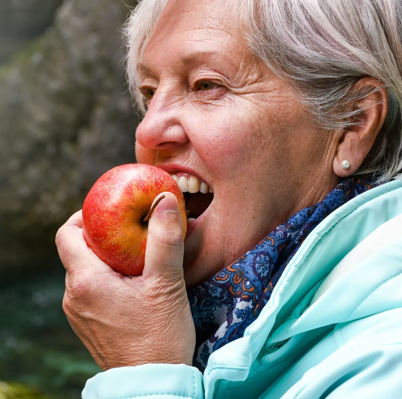 Elderly woman eating a red apple outdoors.