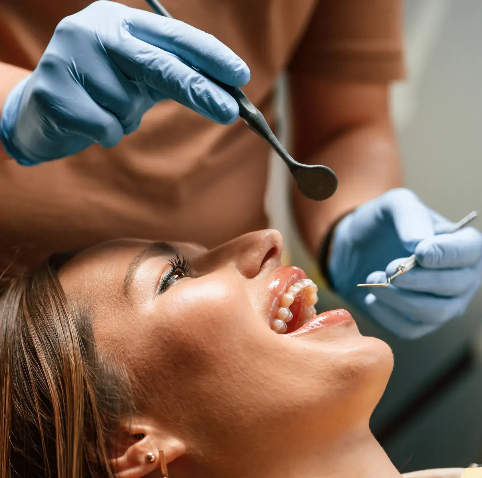 Close-up of a dentist wearing blue gloves examining a smiling woman's teeth with dental tools.