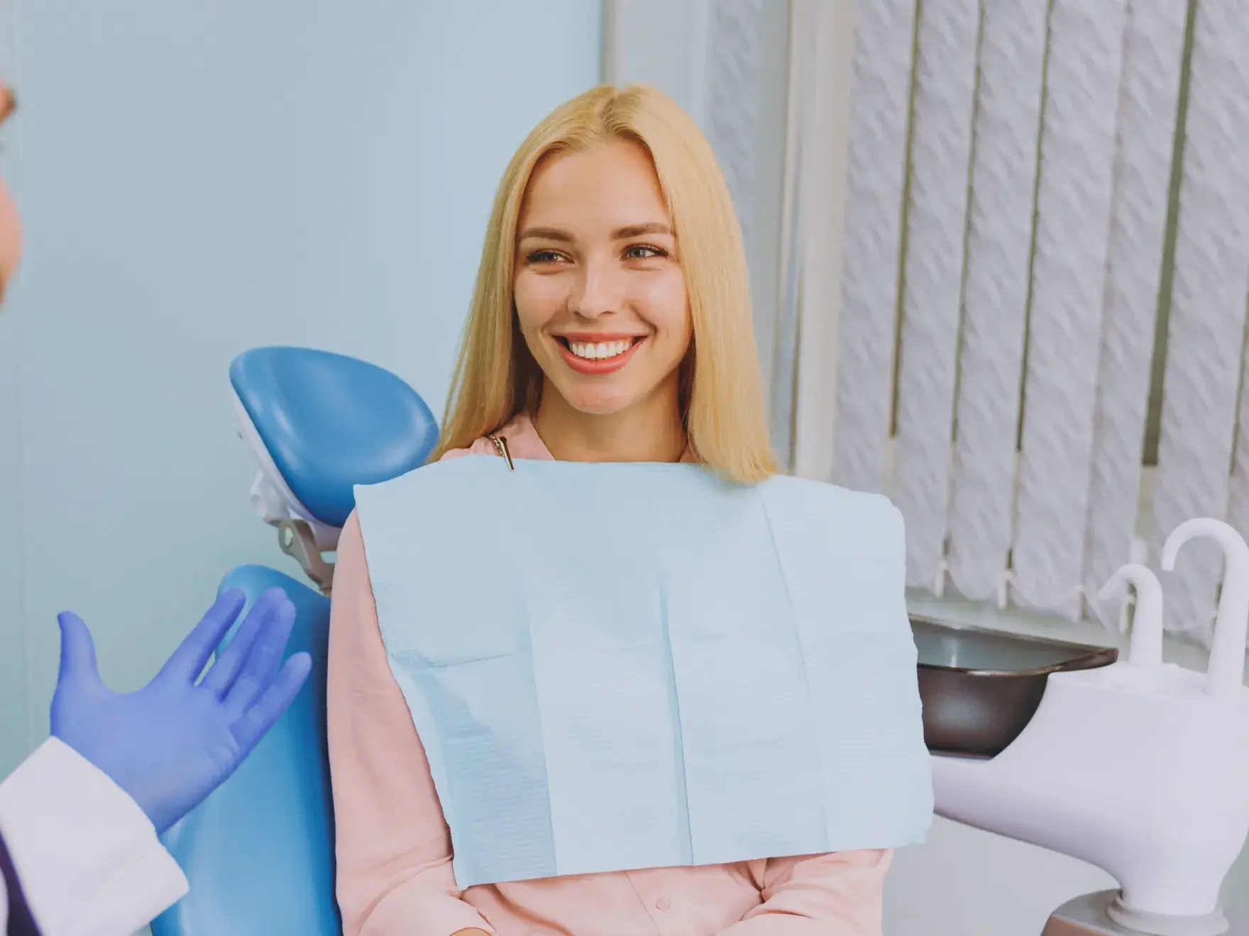 Woman smiling in a dental chair while talking to a dentist wearing gloves.