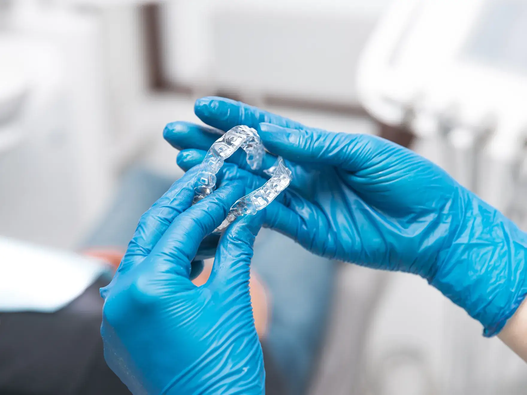 Gloved hands holding a clear dental aligner in a clinical setting.