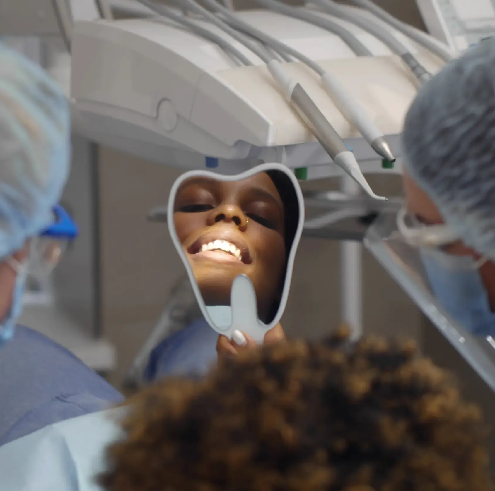 Person in dentist's chair smiling while holding a small mirror, surrounded by dental staff.