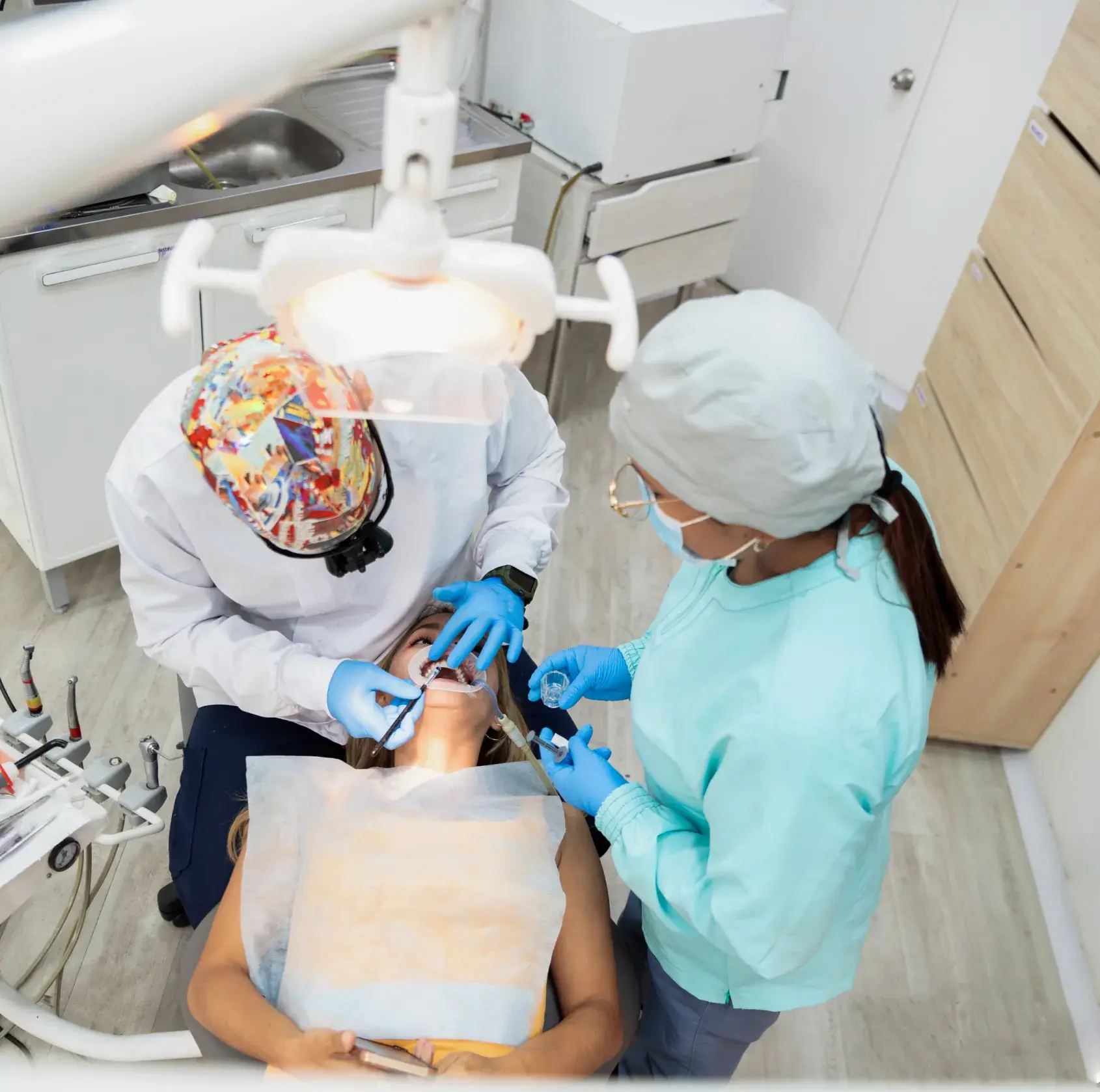 Dental professionals wearing gloves and masks performing a dental procedure on a seated patient in a clinic.