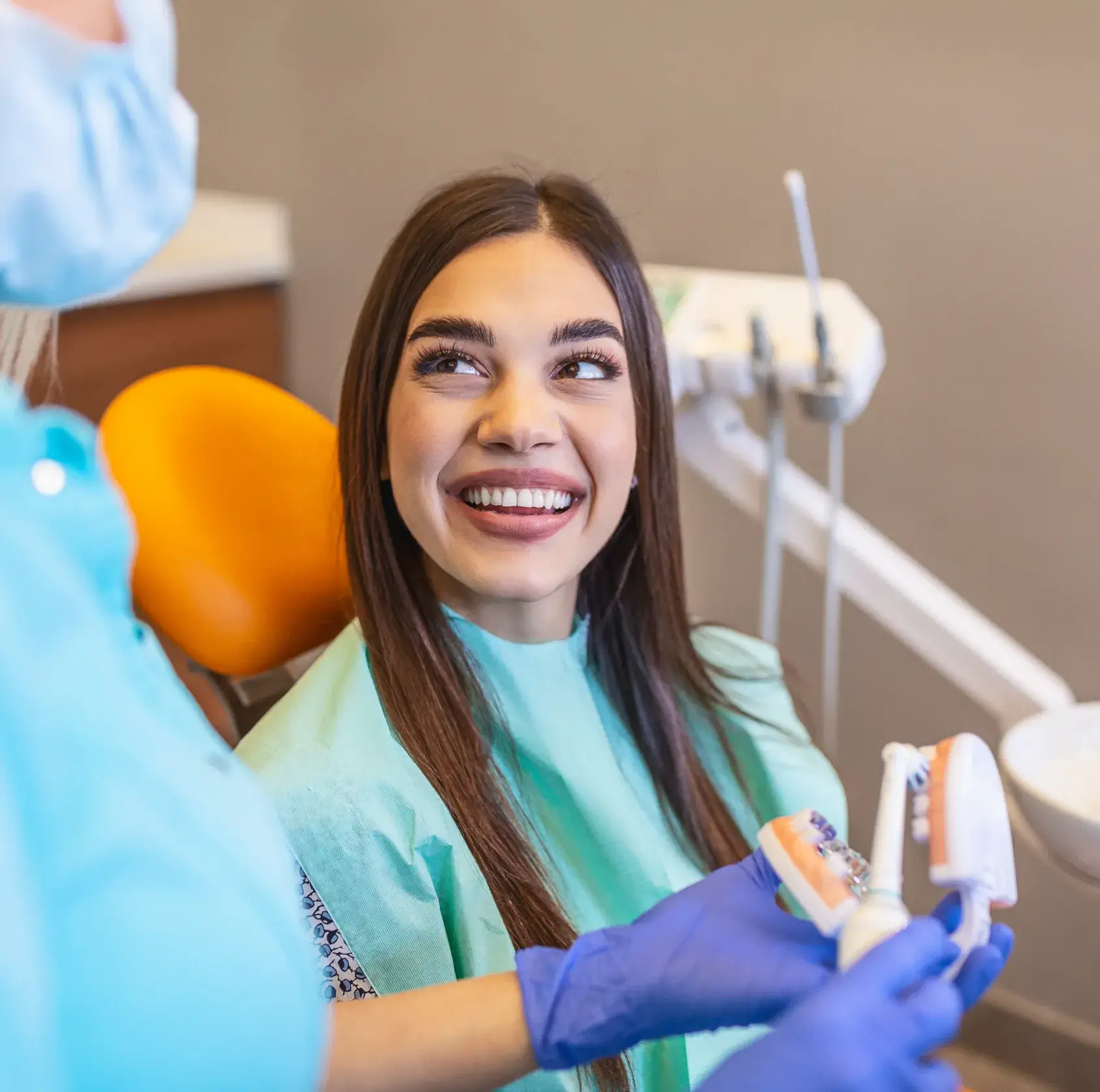 A woman smiles at a dentist holding a dental model and toothbrush.