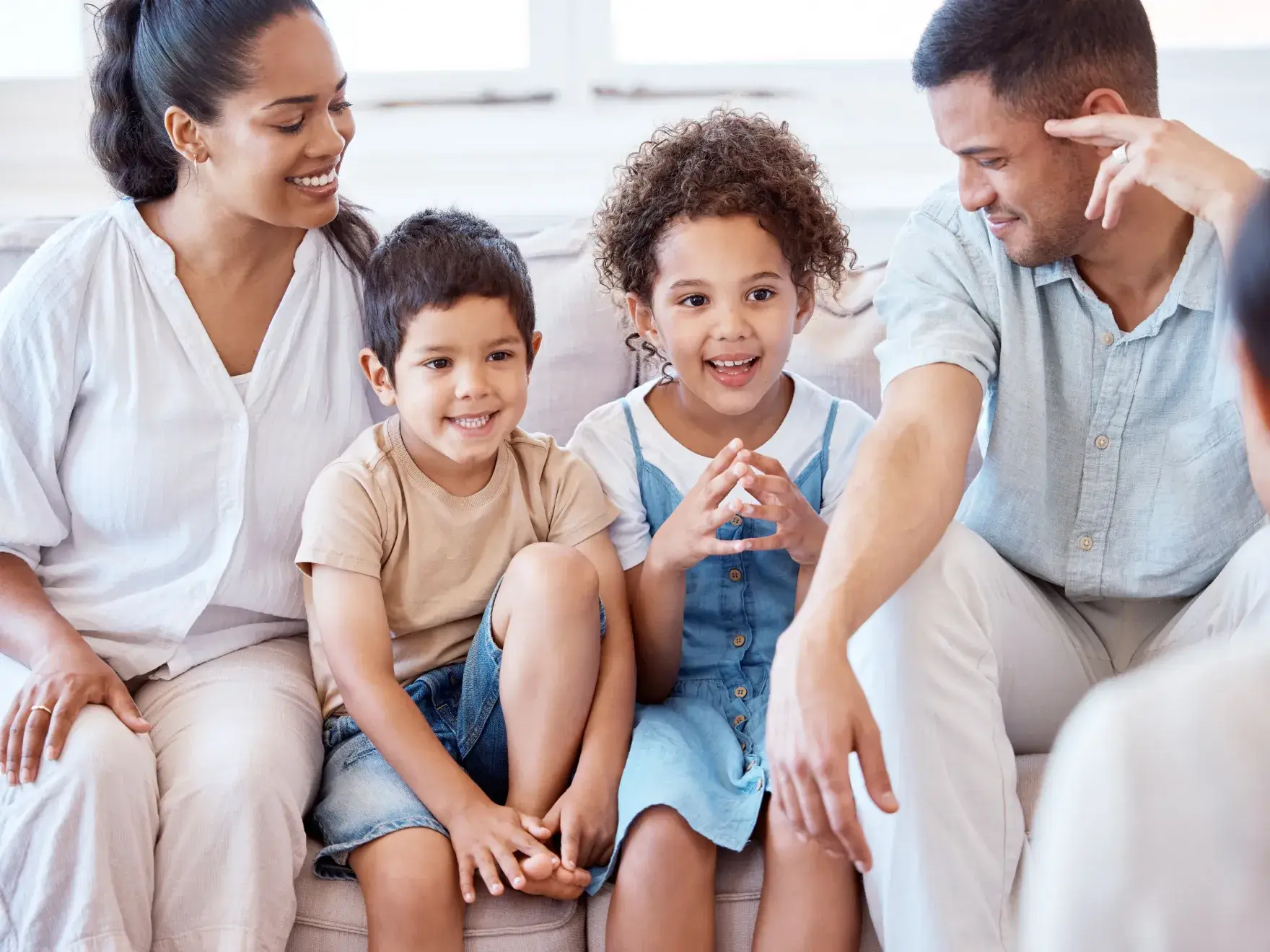 A family of four sits on a couch, smiling and chatting happily together.