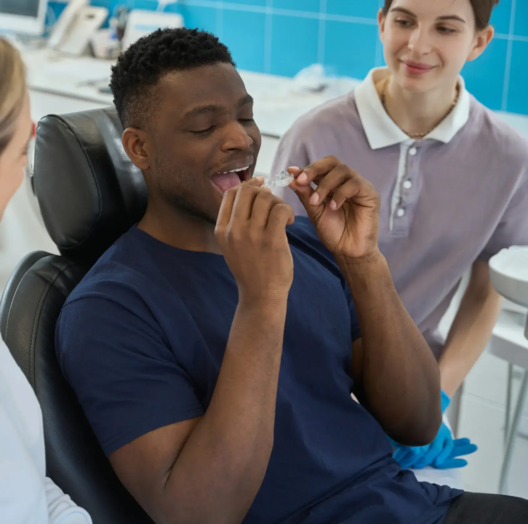A person sitting in a dental chair holds a dental retainer, while two others watch smiling.