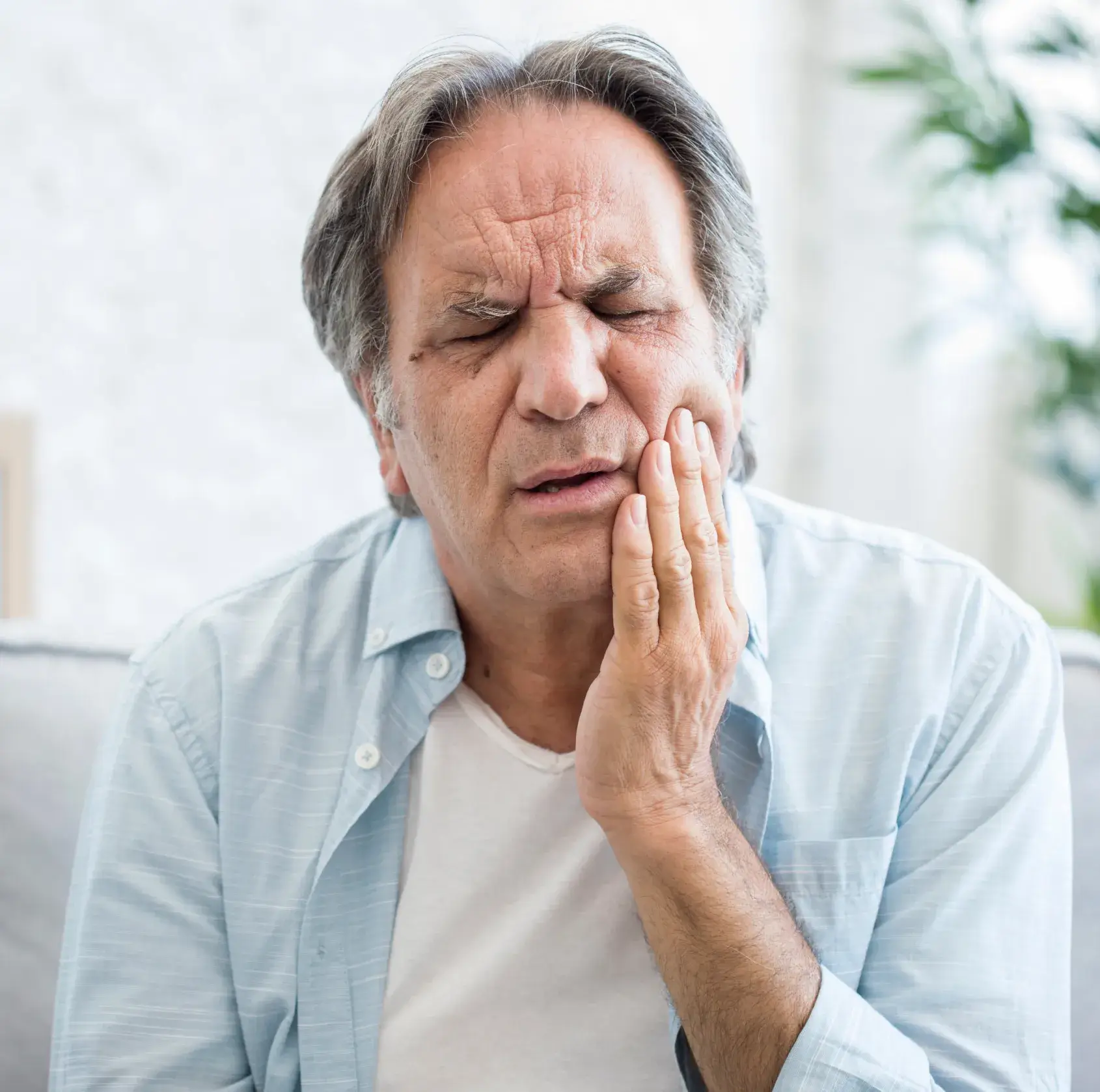 A man sitting and touching his cheek, appearing to have a toothache or facial pain.