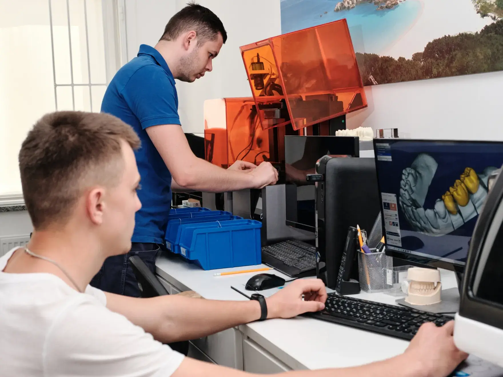Two men working with 3D printers and computer on dental models in an office setting.