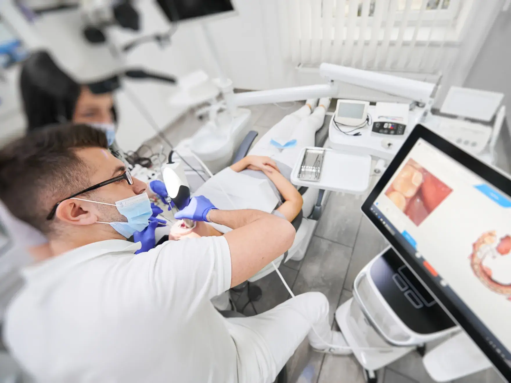 Dentist examines a patient's teeth while viewing images on a computer screen in a dental office.