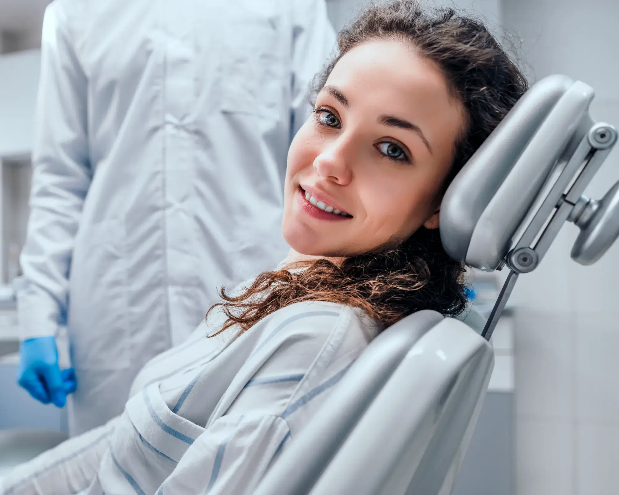 A woman sits in a dental chair, smiling, while a dentist stands nearby.