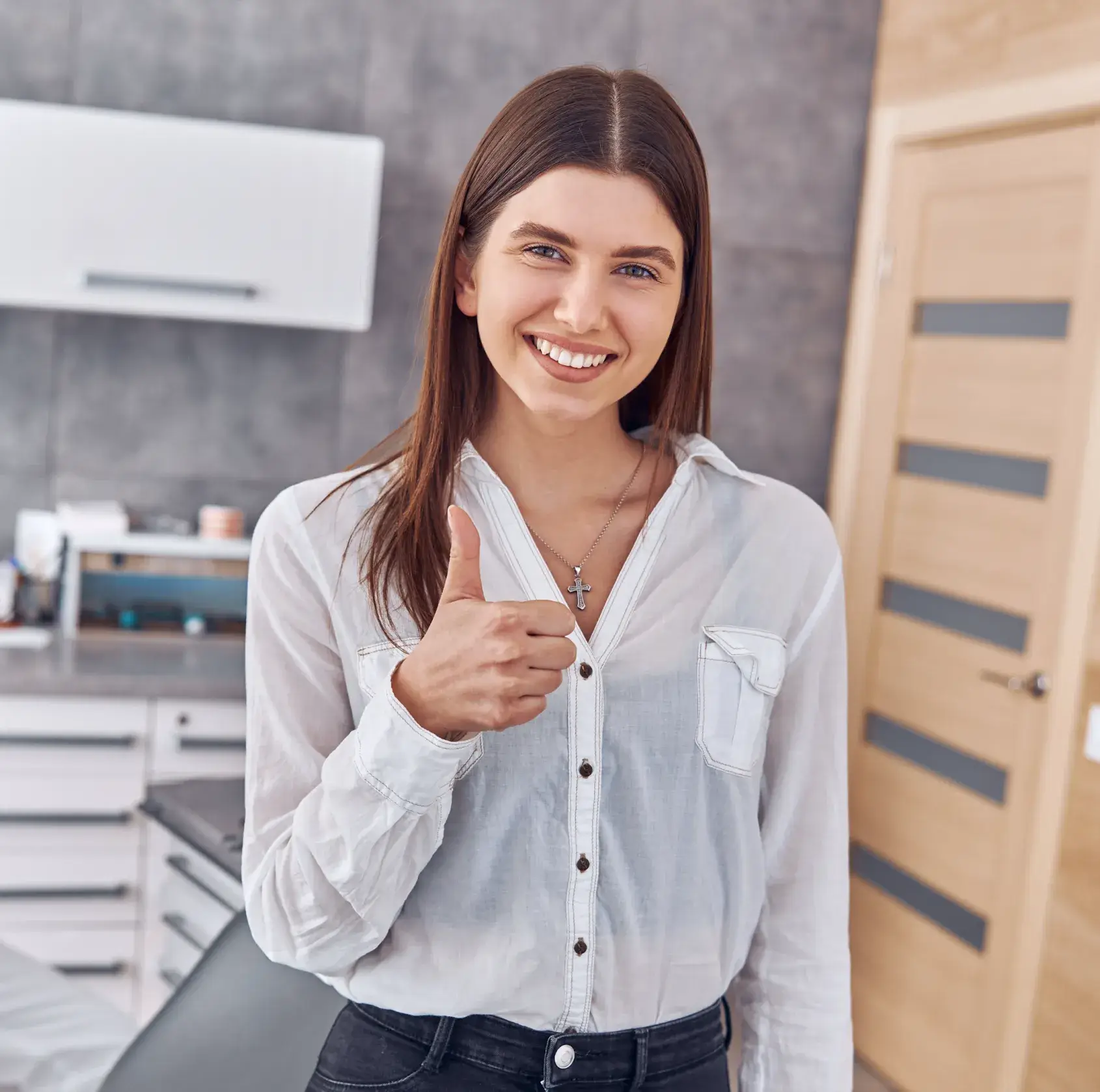 Smiling woman giving a thumbs-up in an office setting.