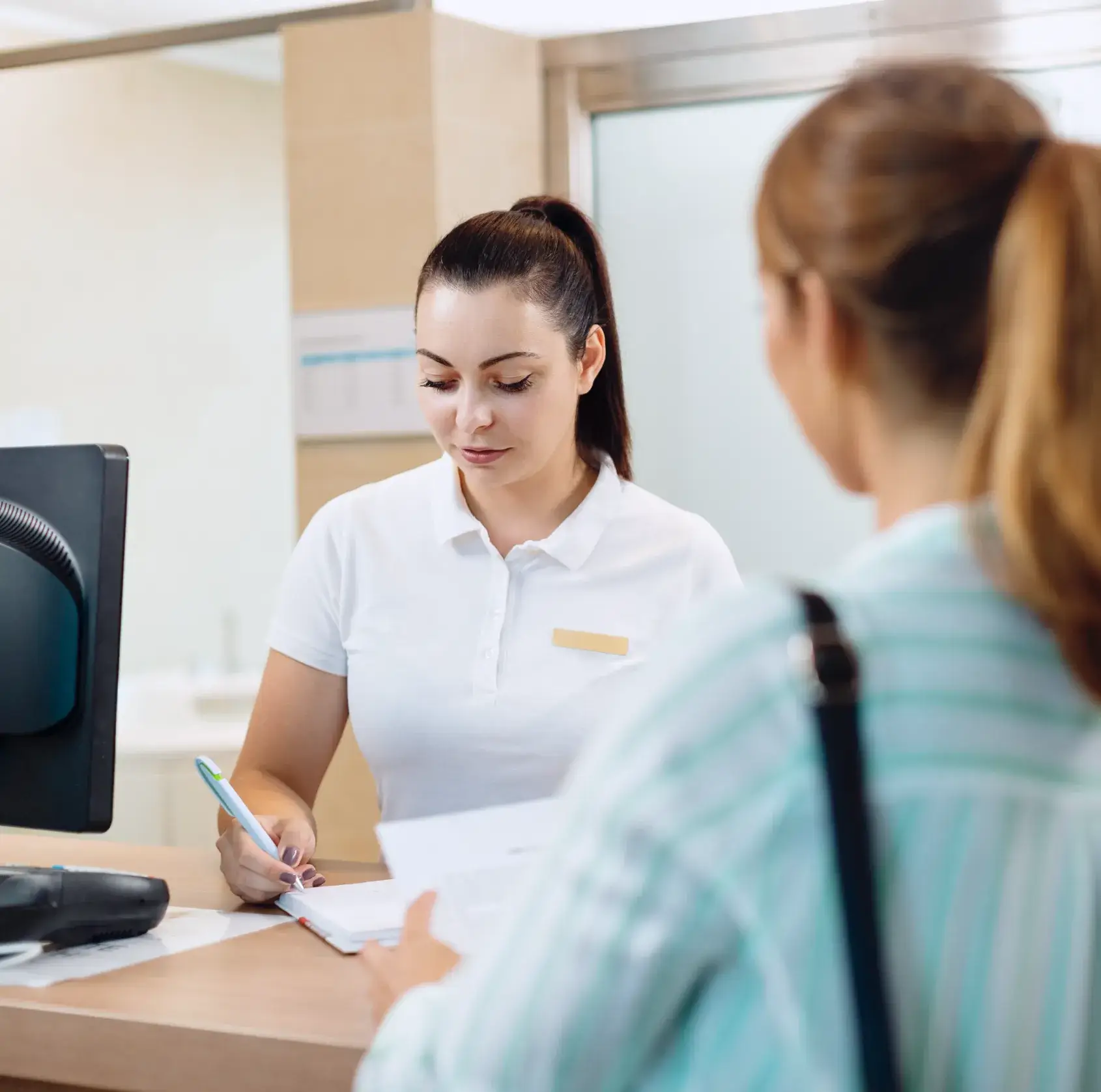 A receptionist in a white shirt helps a customer at the front desk, reviewing paperwork.