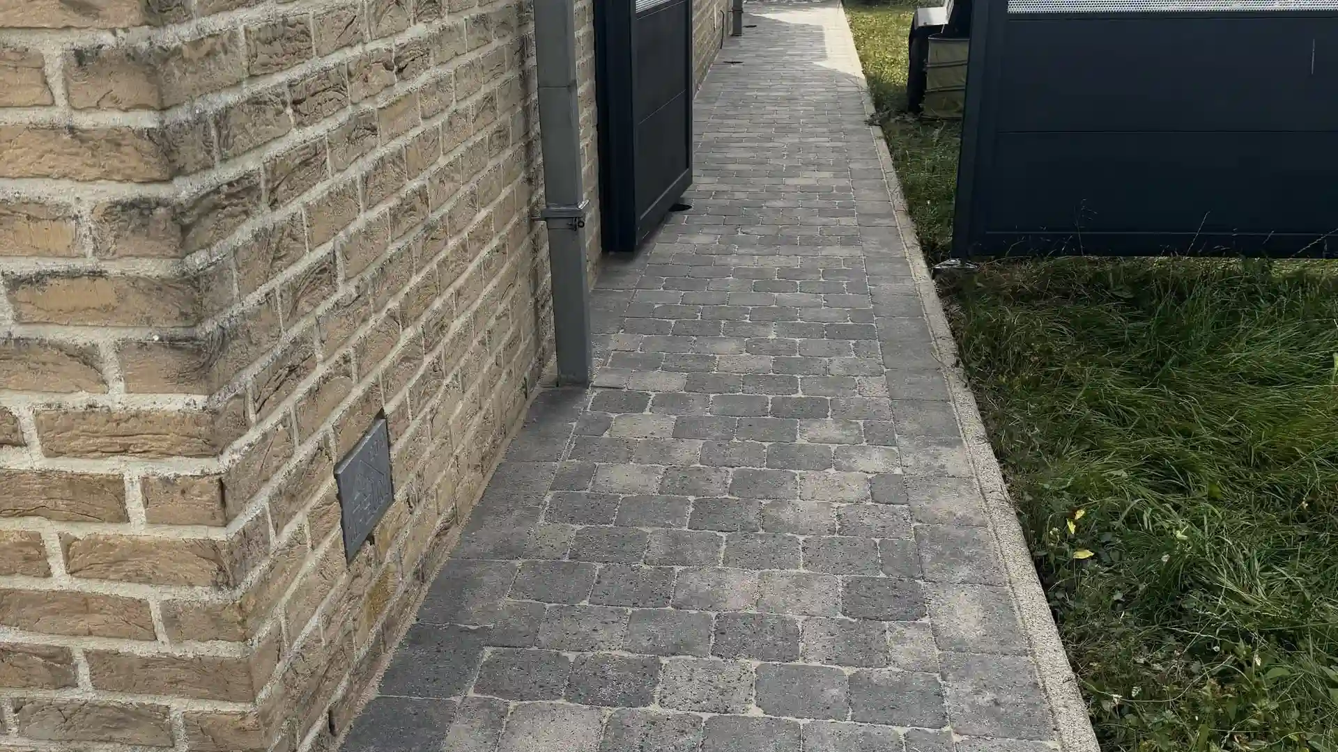 Allée en pavés gris le long d'une façade en briques claires, après nettoyage