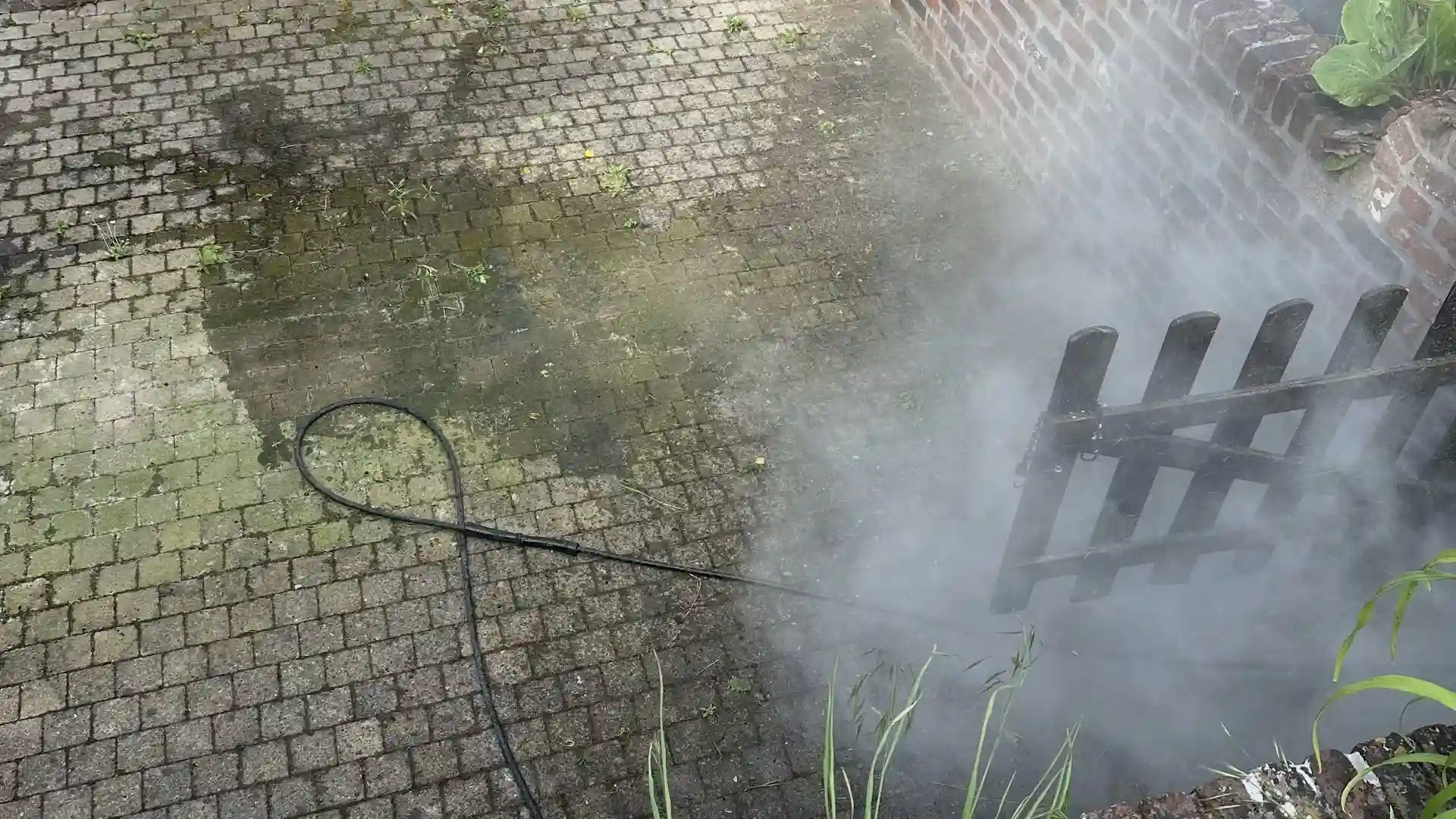 Cour en petits pavés gris clair le long d'un mur en briques, avant nettoyage