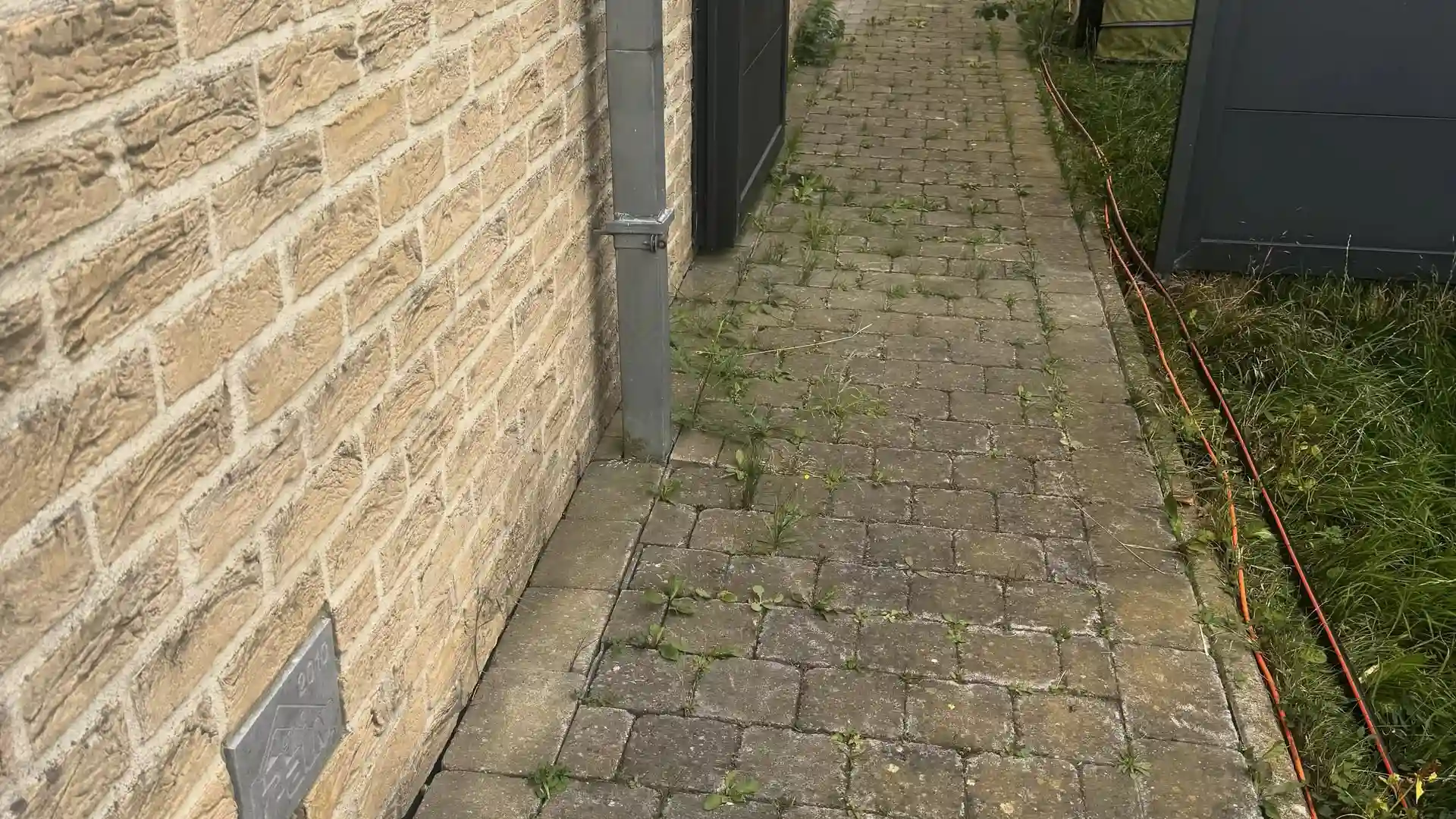 Allée en pavés gris le long d'une façade en briques claires, avant nettoyage